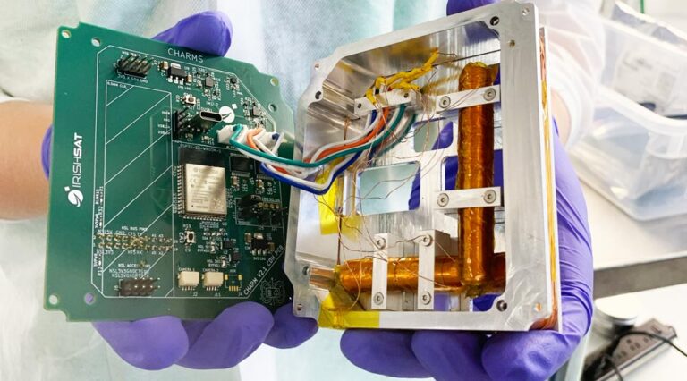purple gloved hands hold components of a mini satellite