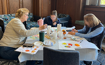 A small group of staff members painting leaves and pumpkins with watercolors during the creative workshop.