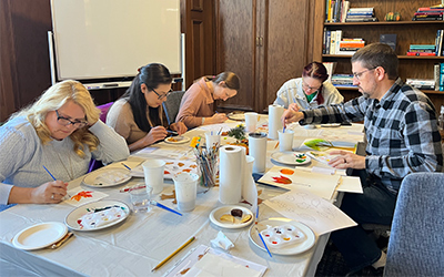College of Engineering staff seated around a table, focused on painting fall-themed watercolor designs.