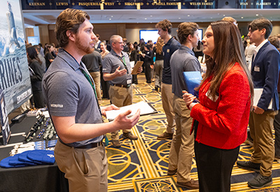 Employer and student engaged in conversation at a booth while other attendees network in the background.