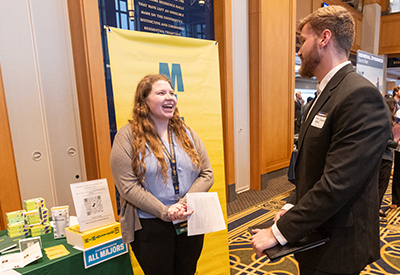 Recruiter smiling while speaking with a student at a table displaying informational materials.