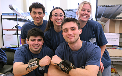 Group of students smiling in a lab space, some wearing and holding wearable prototype devices.