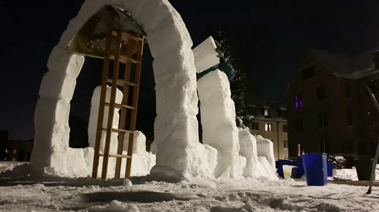 Large snow-and-ice arches take shape at night, supported by a car hood and ladders used as temporary formwork during construction.