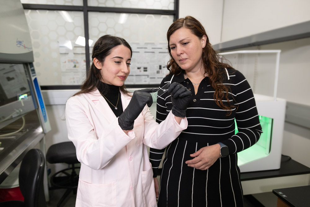 Two women stand side-by-side in a laboratory looking at a microscope slide