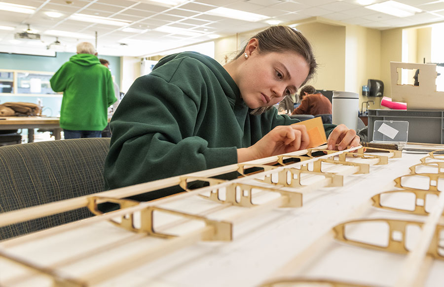 Student in a workspace carefully assembling a wooden aircraft wing structure on a workbench.