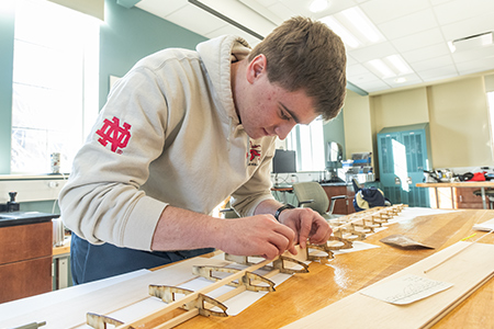 Student concentrates on assembling small wooden aircraft parts at a workbench.