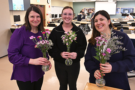 Three women stand together holding small flower arrangements they created.