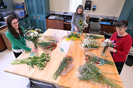 Staff members arrange flowers and greenery together around a large table.