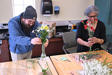 Two staff members place flowers into a vase while working side by side.