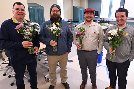 Four staff members stand together holding small flower bouquets and smiling.
