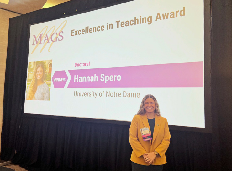 Hannah Spero stands in front of a presentation screen. She is wearing a yellow blazer.