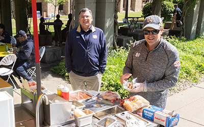 A staff member serves hot dogs from an outdoor hot dog stand during the Staff Appreciation Lunch.