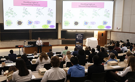 A student presents research on drug delivery to an audience in a lecture hall.
