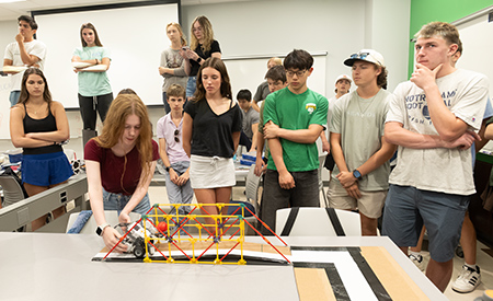 Students watch a model bridge test during a hands-on engineering activity.