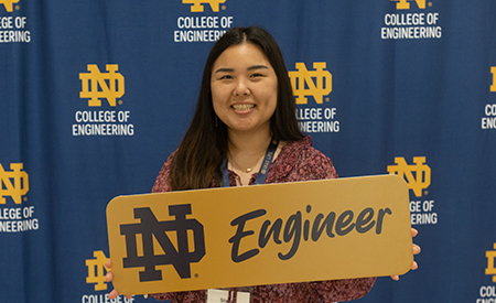Graduate student poses for a photo with a College of Engineering “ND Engineer” sign.