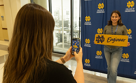 Graduate student takes a photo of another student posing with an “ND Engineer” sign.