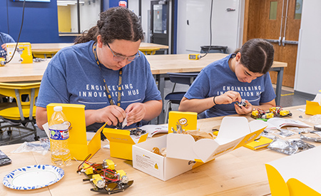 Two high school students assemble small robotic cars at a workbench in the Engineering Innovation Hub.