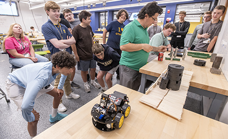High school students watch as an instructor demonstrates weight on a wooden bridge.