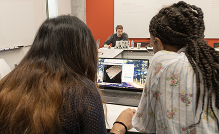 Two students examine microscopy images on a laptop during a research session.