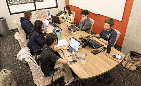 Students and researchers work together on laptops around a conference table.