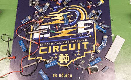 An assortment of electrical components and circuit-building materials is arranged on a Notre Dame Electrical Engineering mat.