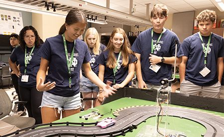 Students watch slot cars race around a model track during a hands-on electrical engineering activity.