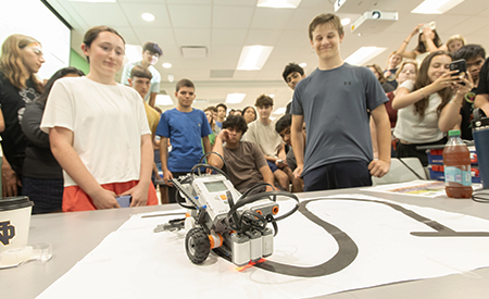 Students watch a small robot navigate a course during a robotics activity.