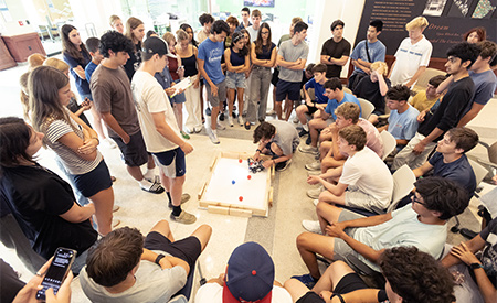 Students gather around a tabletop course to watch a small robot in action.