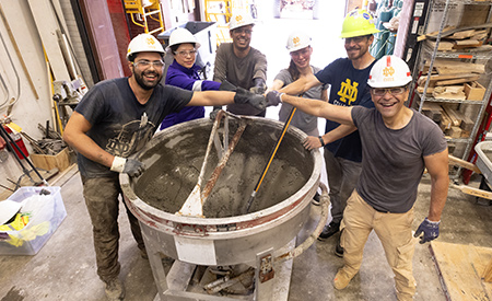 A group of researchers gathers around a concrete mixer during casting in the Structural Systems Laboratory.
