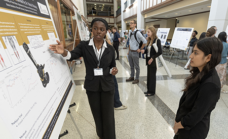 A student discusses her research poster with another symposium attendee.