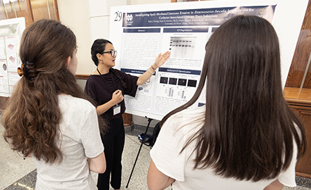 A student explains a research poster to two attendees at the symposium.
