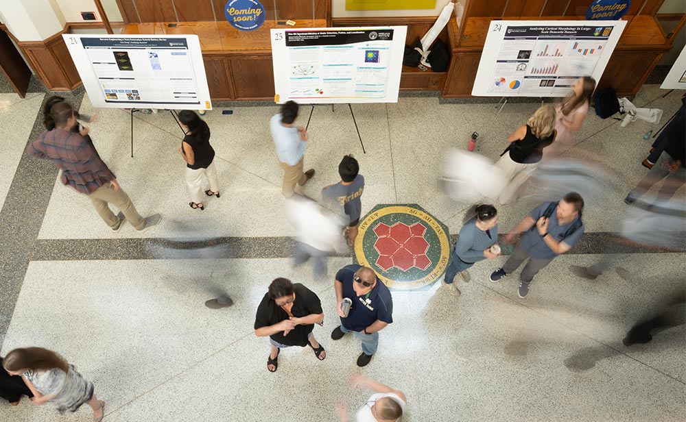 Students walk among research posters during the Summer Undergraduate Research Symposium.