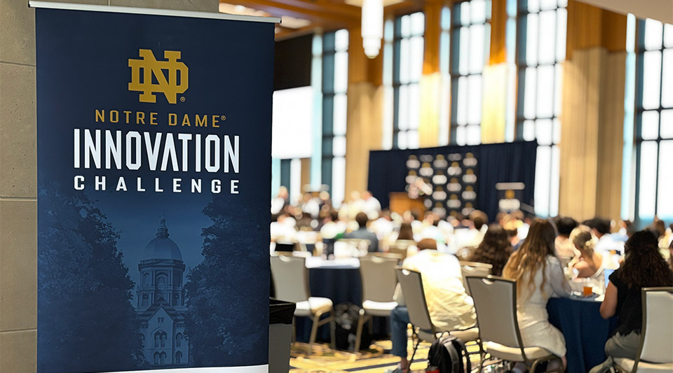 A Notre Dame Innovation Challenge banner stands in the foreground while students gather at tables in the Dahnke Family Ballroom.
