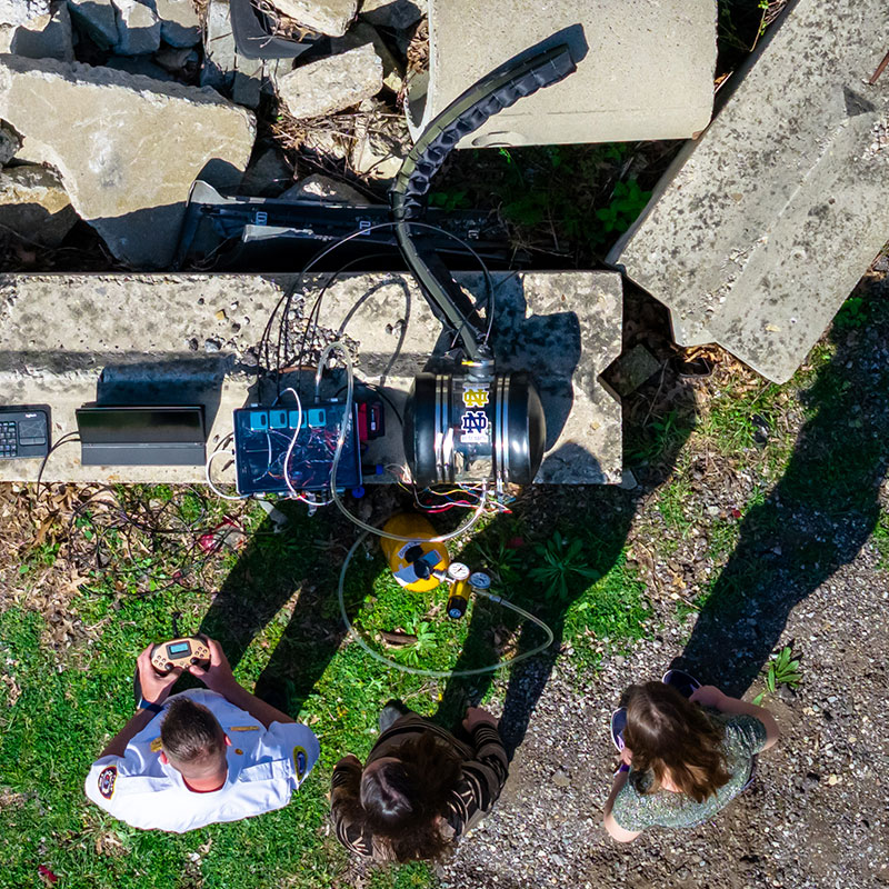 Aerial view of two Notre Dame engineers and a firefighter preparing a vine robot to explore a pile of concrete rubble.